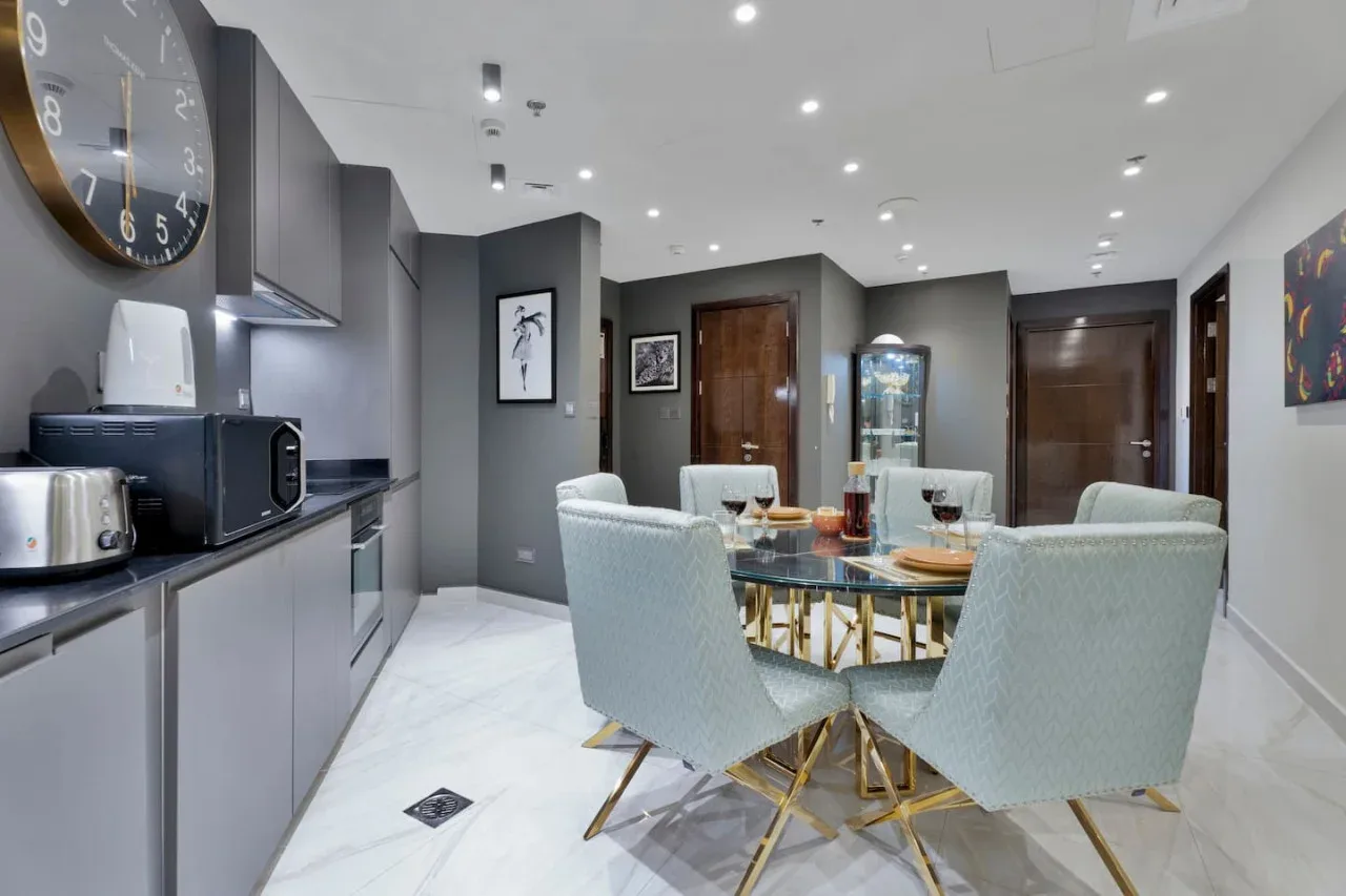 A dining area with a glass table and upholstered seating beside a kitchenette.