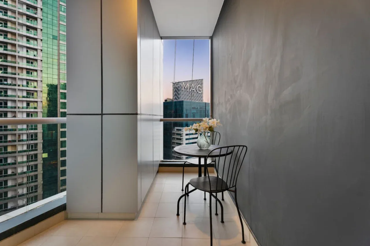 A narrow balcony with seating and a small table overlooks nearby buildings.