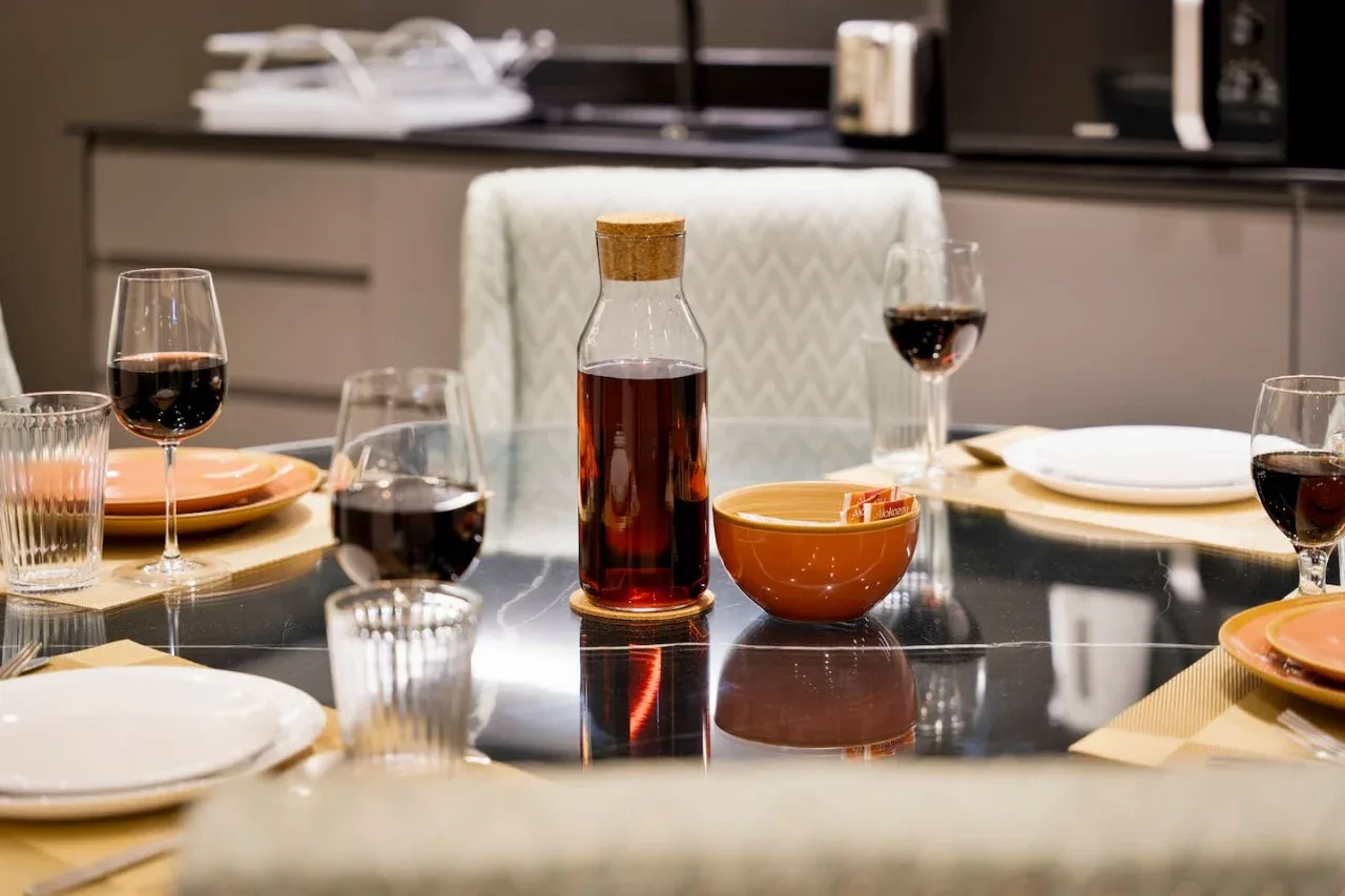 A dining table is set with plates, glasses, and a bottle of sauce.