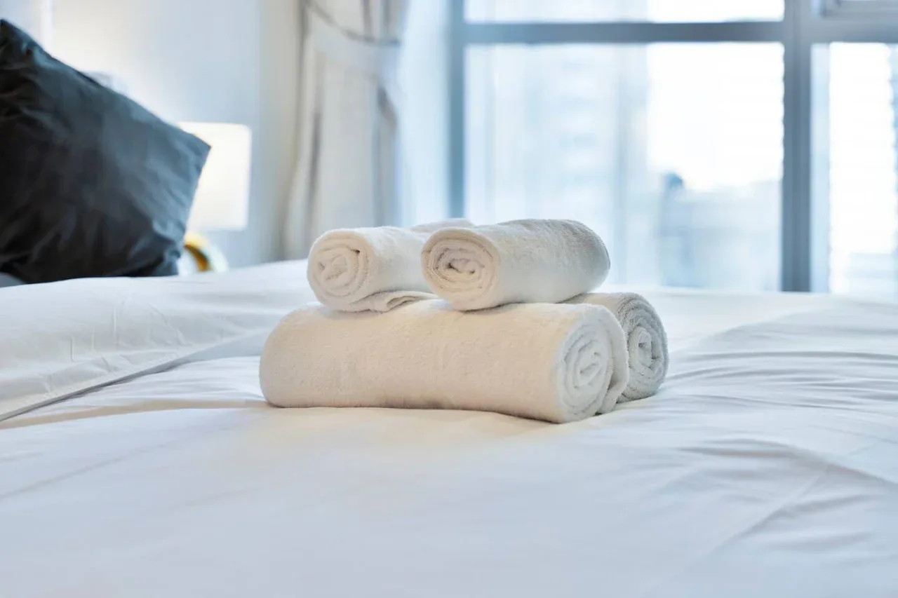 A bedroom with neatly folded white towels on a bed beside a large window.