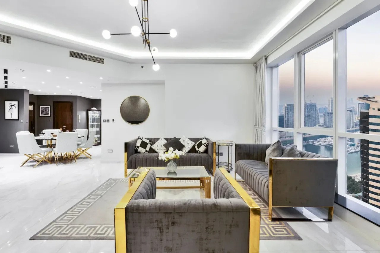 A bright living room with seating beside floor-to-ceiling windows overlooking the city.
