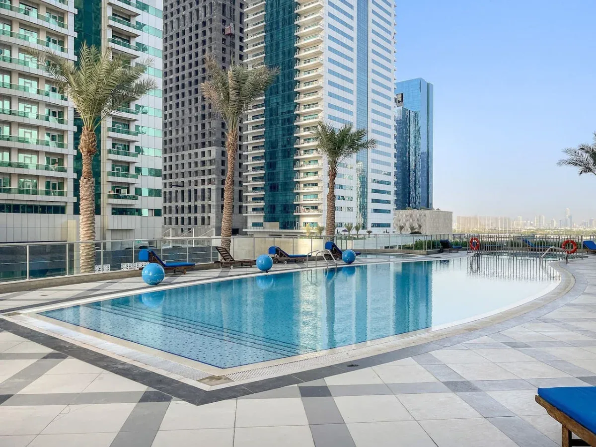 A rooftop swimming pool sits beside modern high-rise buildings.