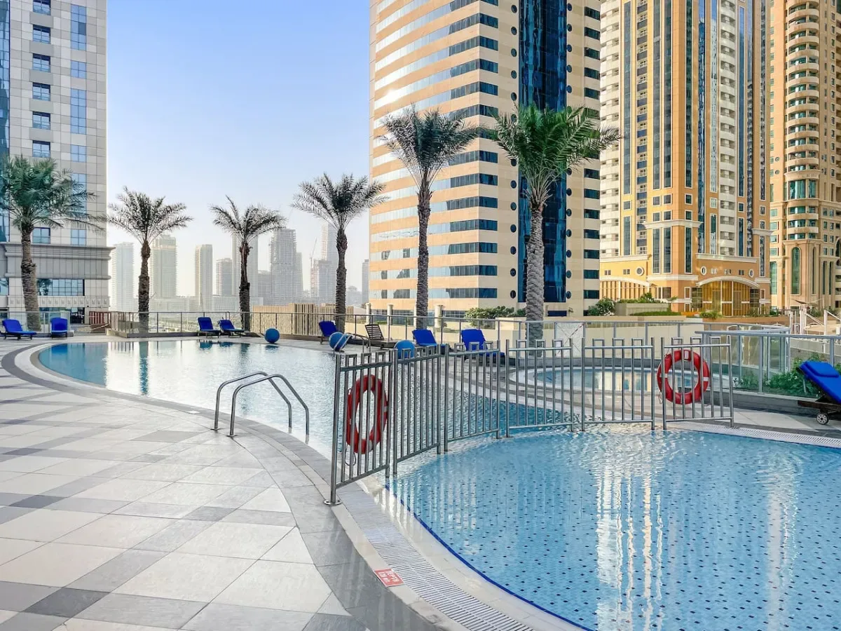 An outdoor pool area with tiled deck, seating, and tall buildings in the background.