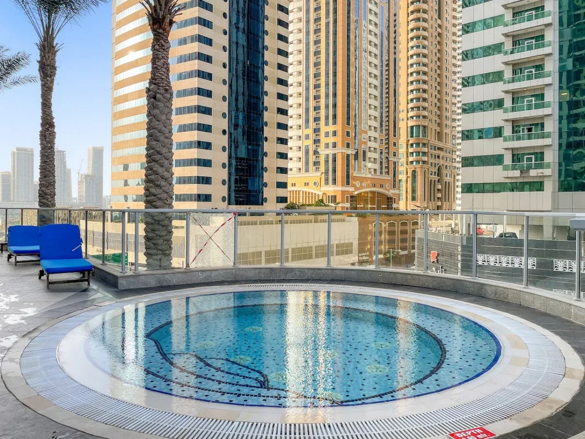 A rooftop pool sits beside high-rise buildings, with blue seating nearby.