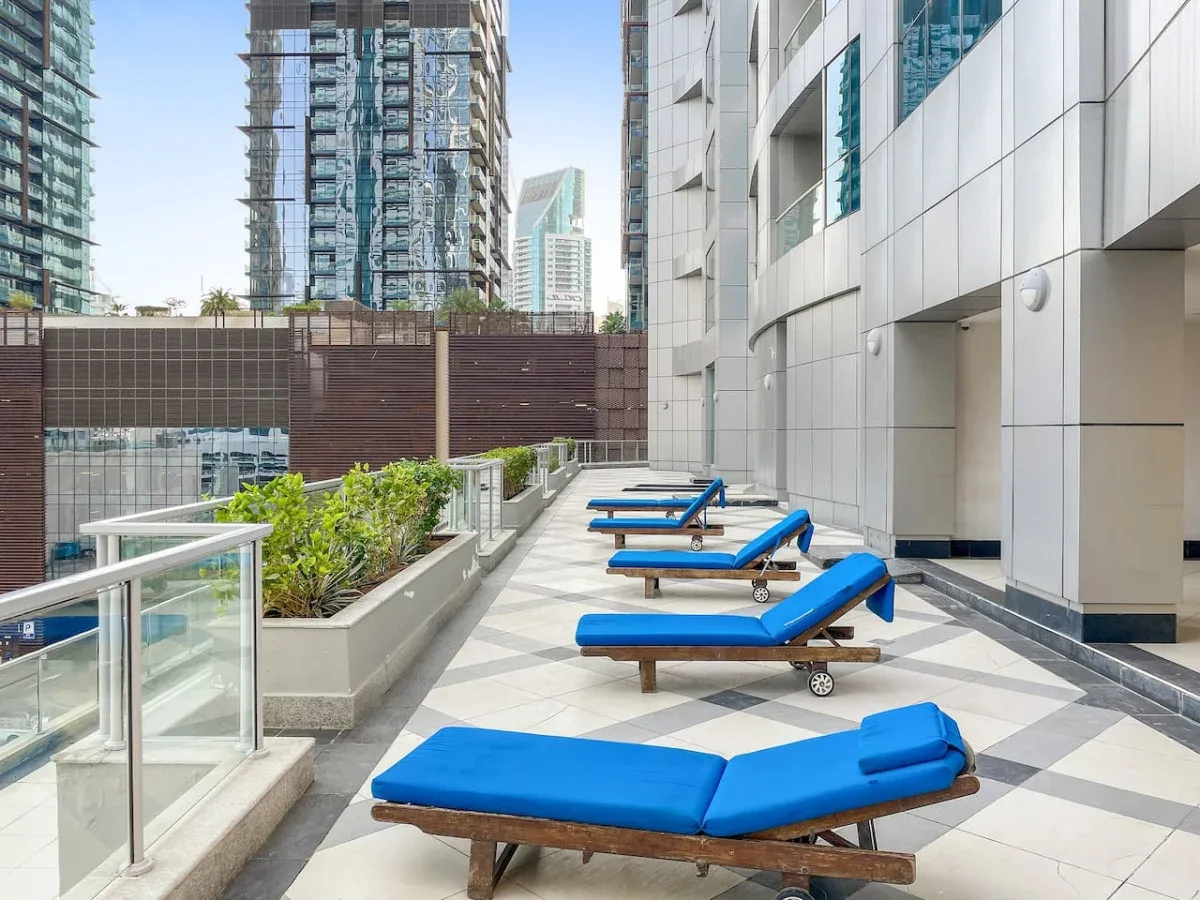 An outdoor terrace with blue-cushioned loungers beside planters and glass railings.