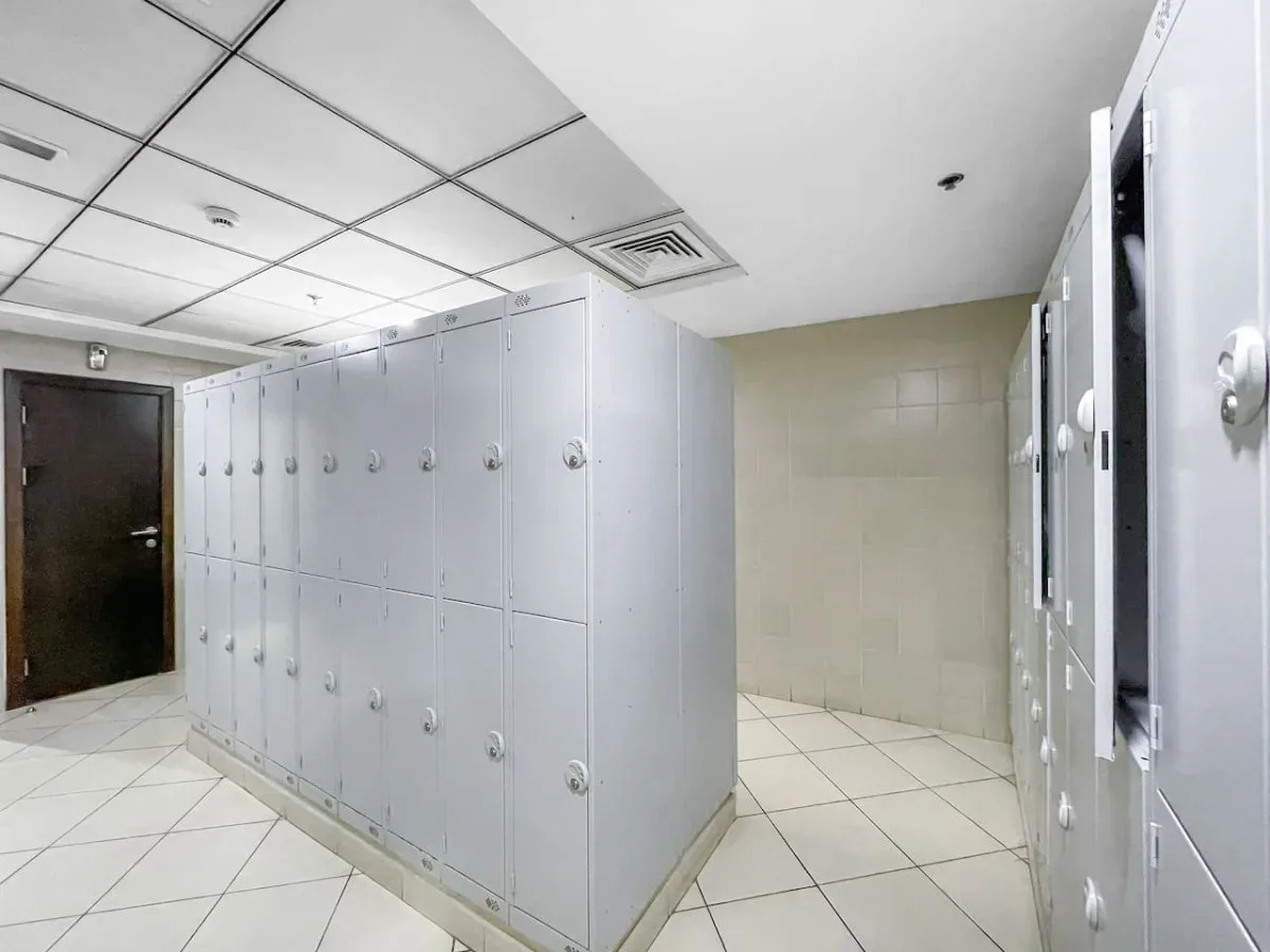A tiled locker room with rows of lockers and a dark door.