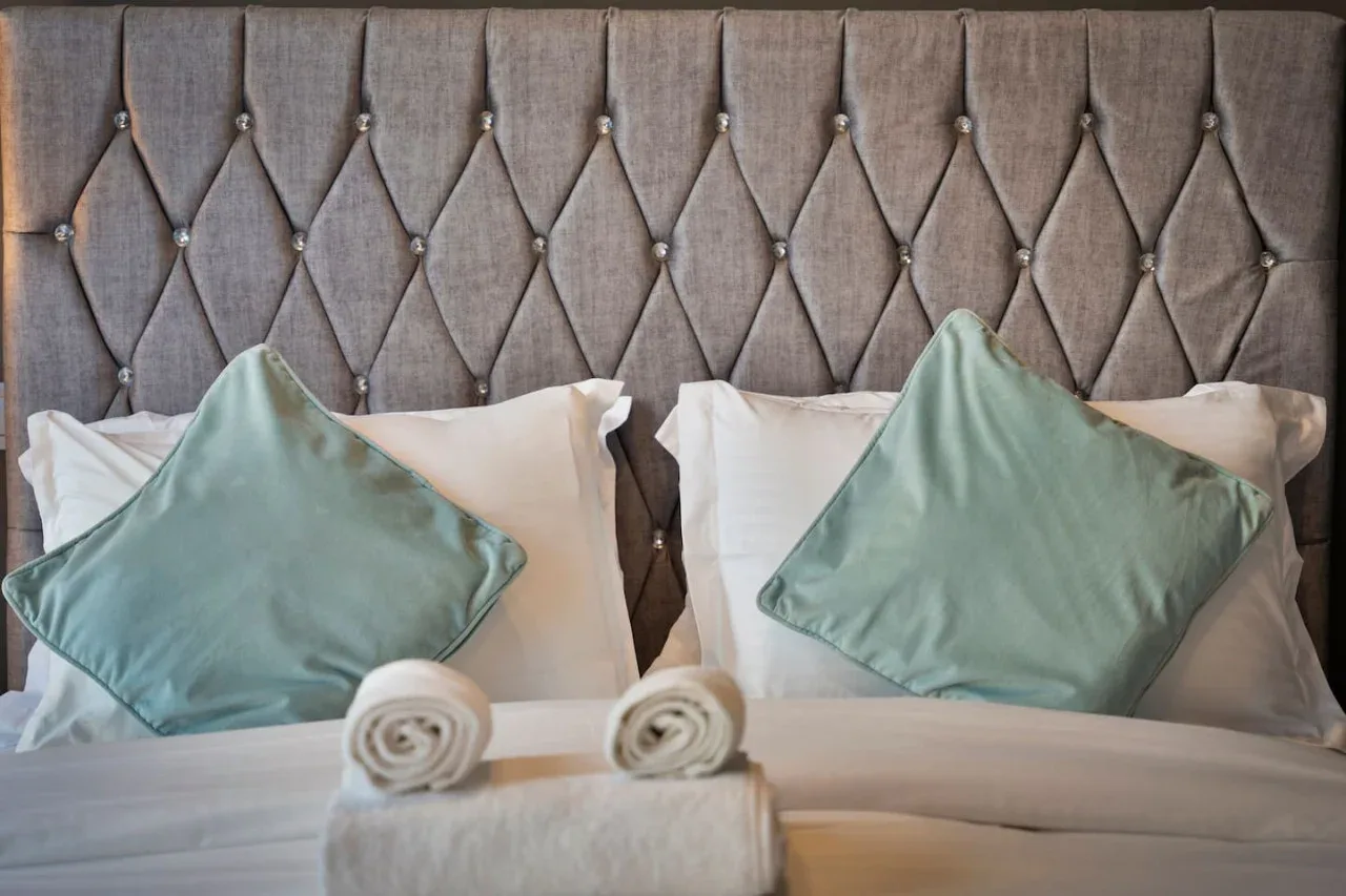 A bed with a tufted upholstered headboard, white bedding, and pale green cushions.