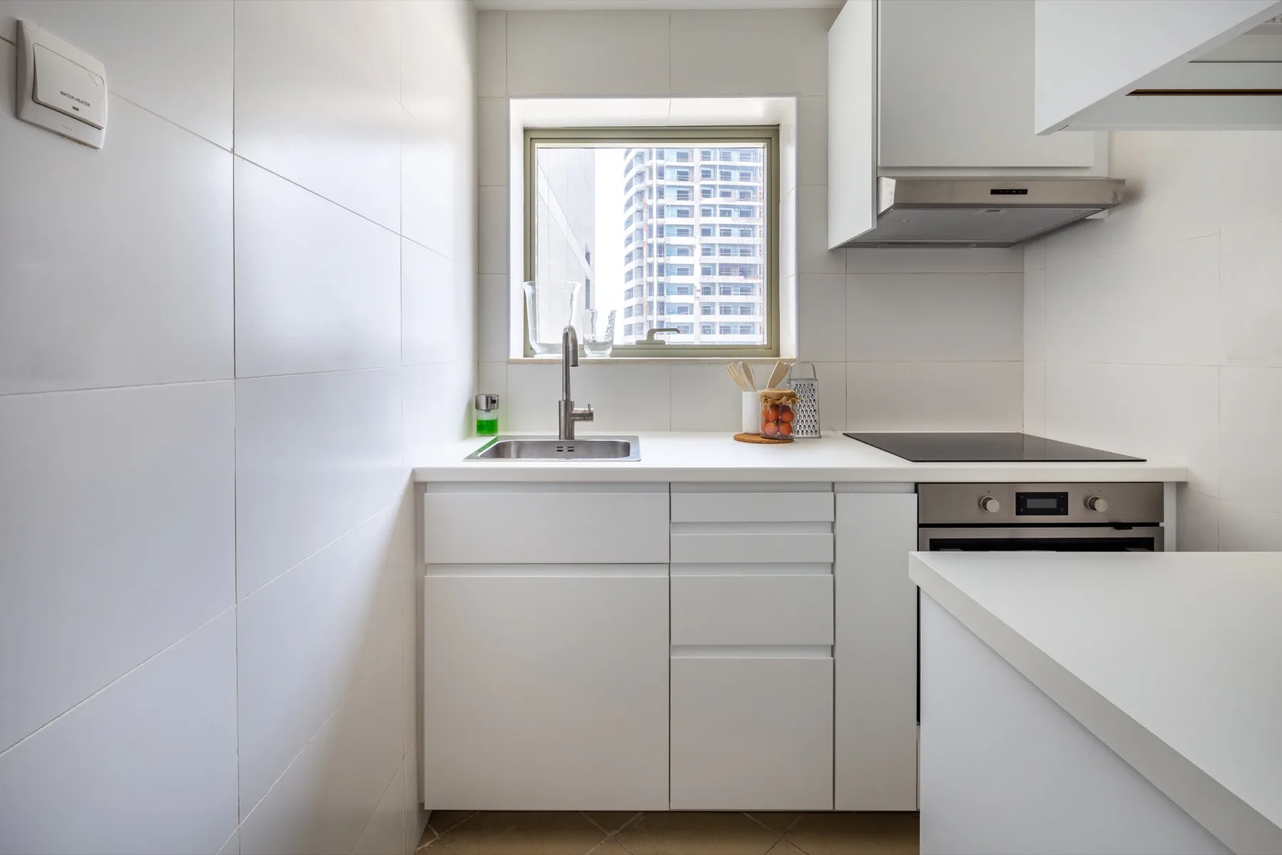 Una cocina blanca y luminosa con una ventana sobre el fregadero y una placa de cocina.