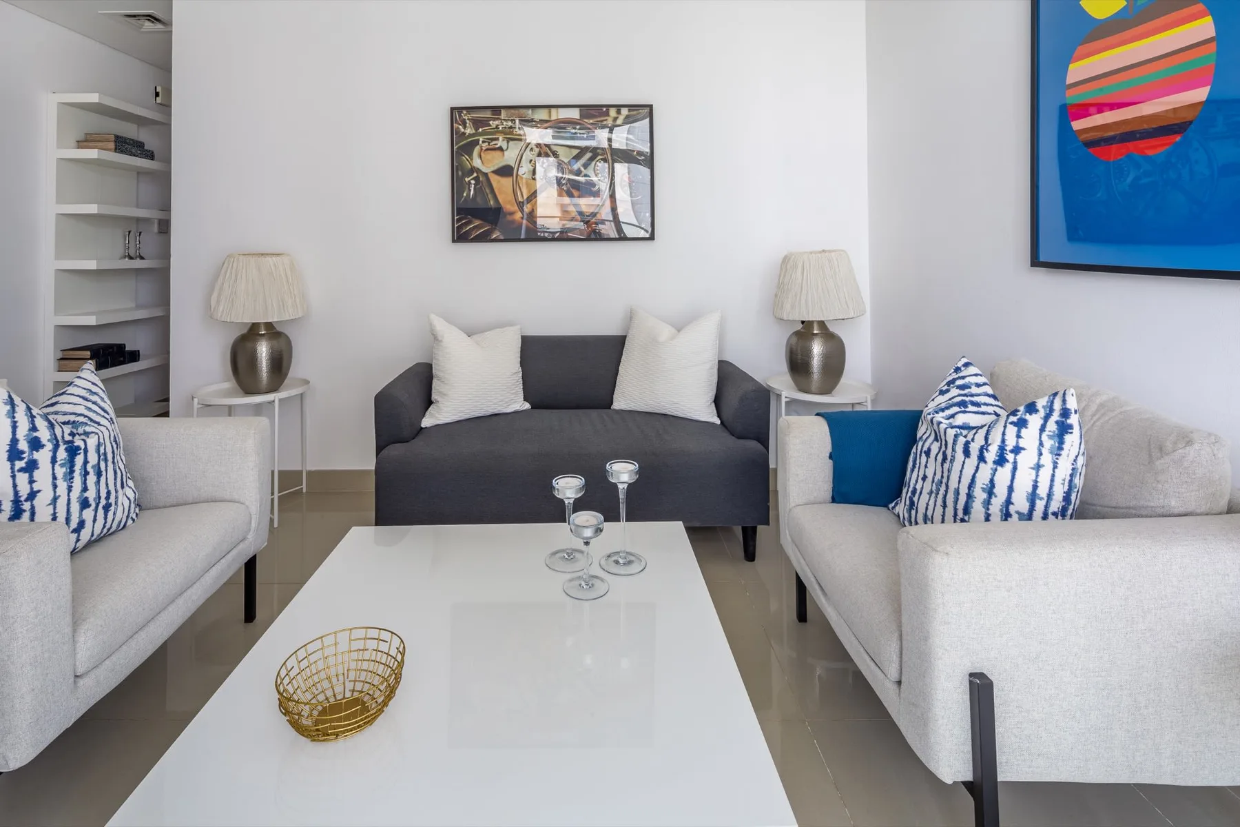 Una sala luminosa con asientos grises, una mesa de centro blanca y arte colorido en la pared.