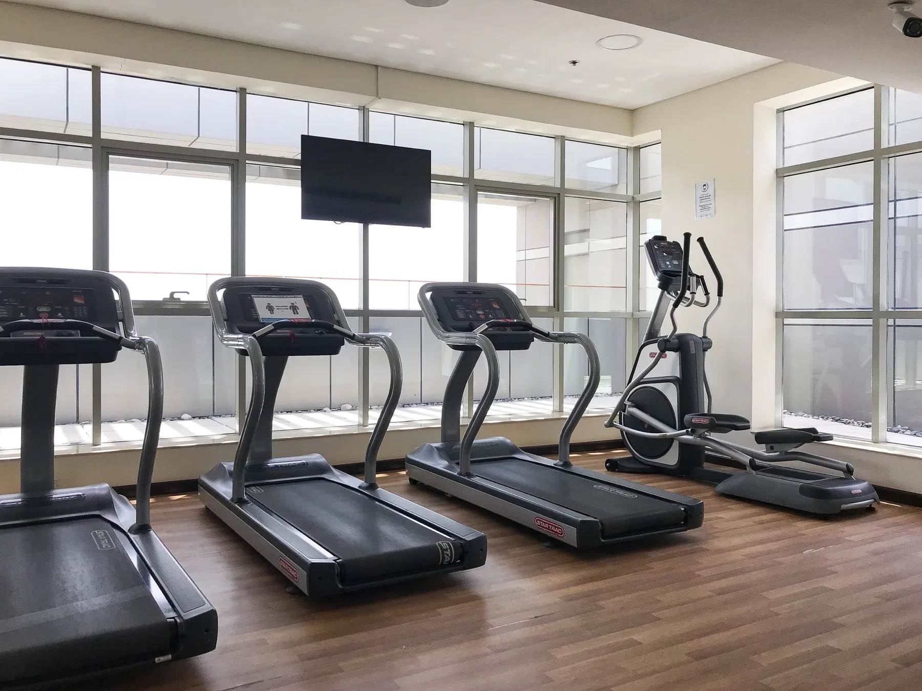 Una luminosa sala de ejercicio con cintas de correr y otros equipos junto a grandes ventanales.