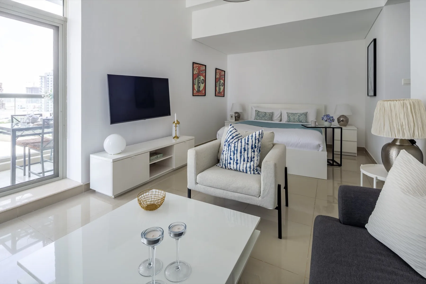 Una luminosa sala de estar tipo estudio tiene una cama, asientos y un televisor montado en la pared.