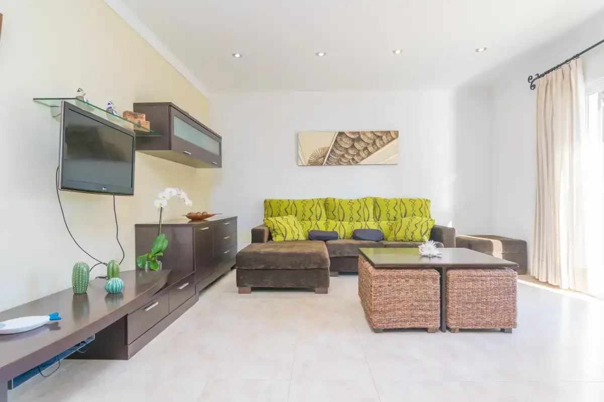 A bright living room with seating, a coffee table, and a wall-mounted television.