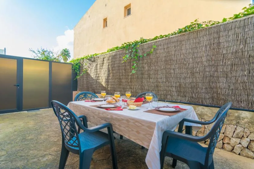 An outdoor dining area with a table set beside a tall woven fence.