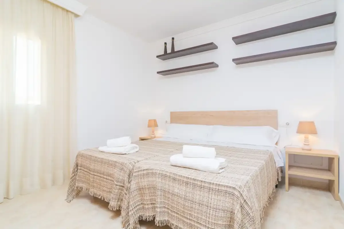 A bright bedroom with a double bed, folded towels, and bedside lamps.