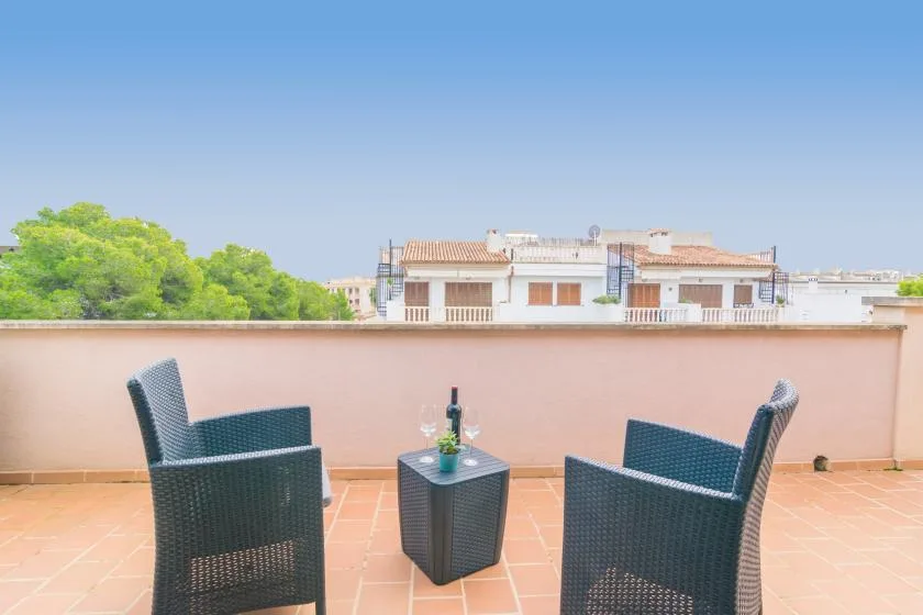 A rooftop terrace has two outdoor seats and a small table beside a low wall.
