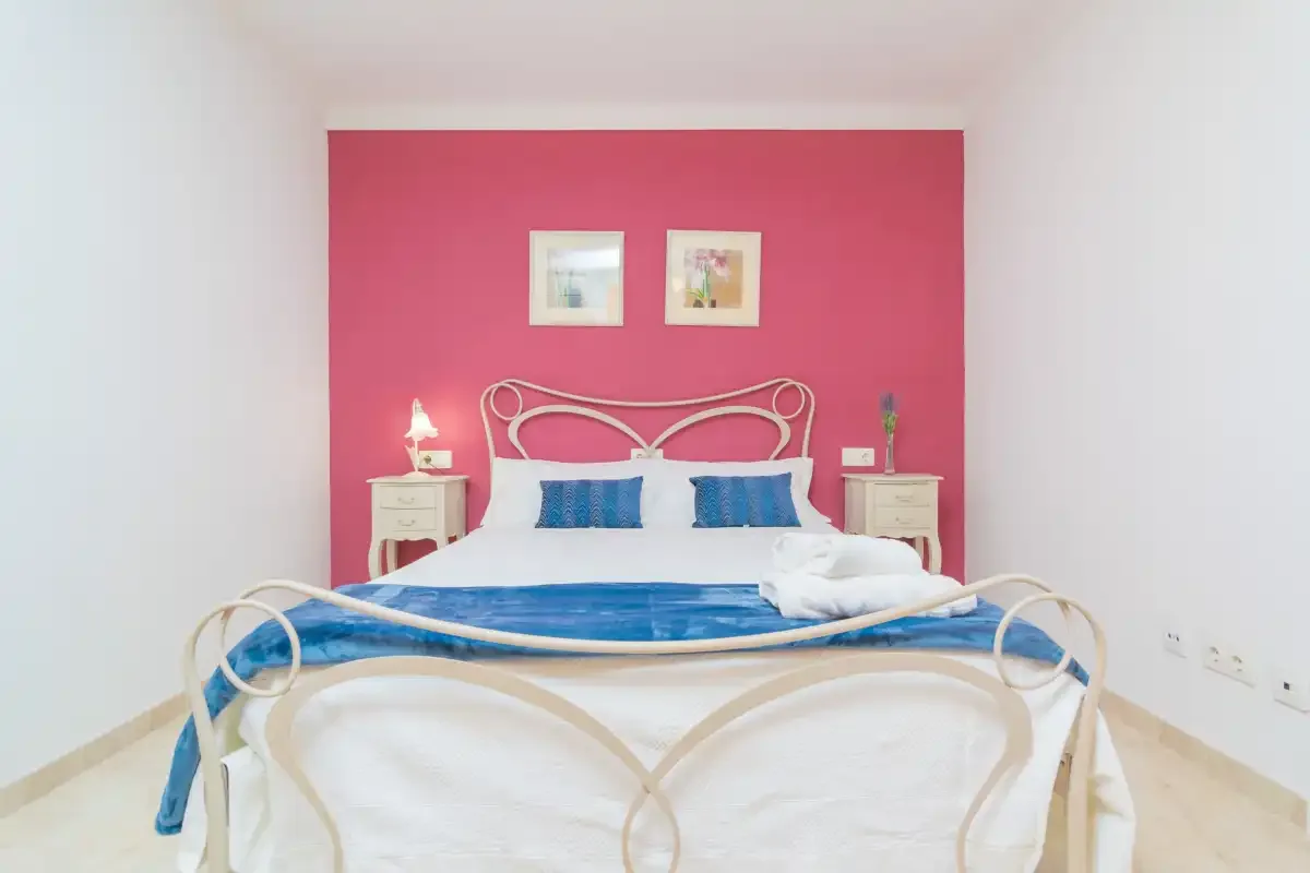 A bedroom with a white bed set against a bright pink wall.