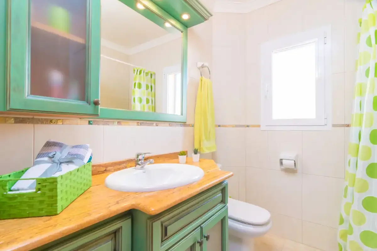 A bathroom with a sink vanity, toilet, and bright green cabinetry.