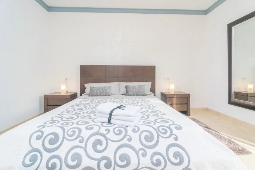 A bedroom with a bed dressed in white patterned bedding and bedside tables.