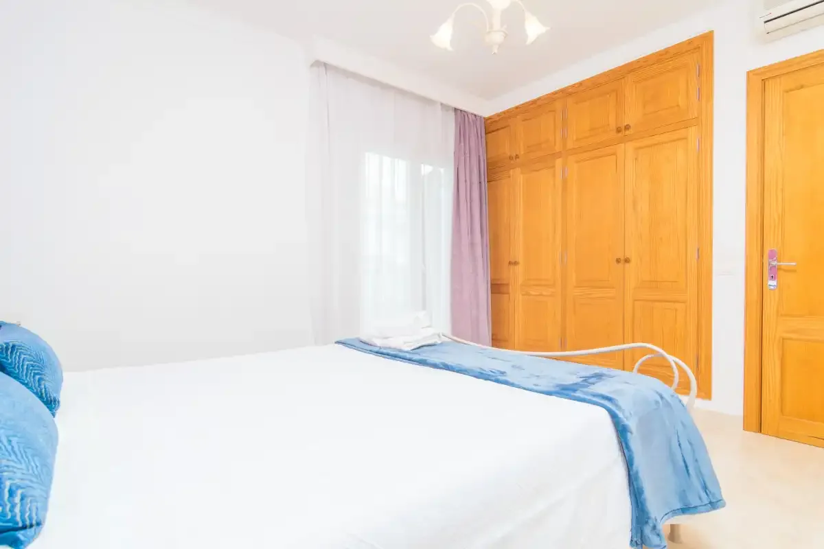 A bedroom with a bed covered in white bedding and blue accents.