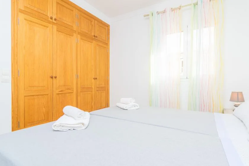A bedroom with a neatly made bed, wooden wardrobes, and a bright curtained window.