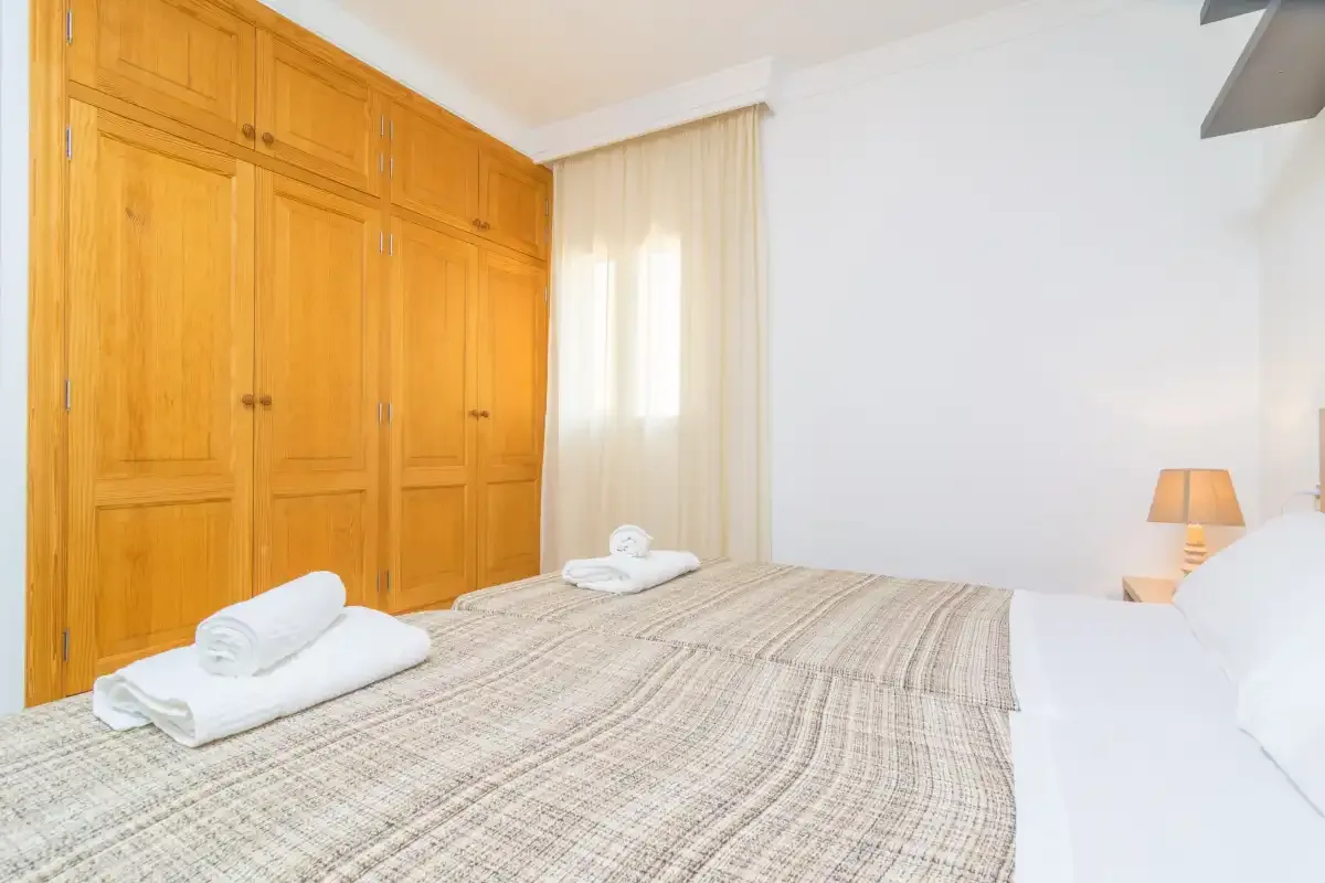 A bedroom with a made bed, wooden wardrobes, and a curtained window.