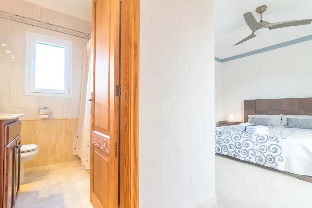 A bedroom with a bed and ceiling fan, viewed through an open doorway.