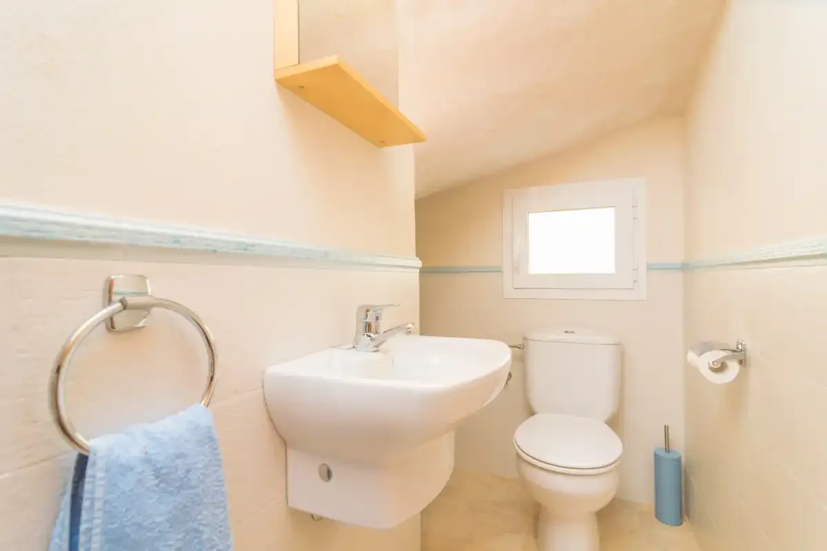 A small bathroom with a wall-mounted sink and toilet beneath a window.