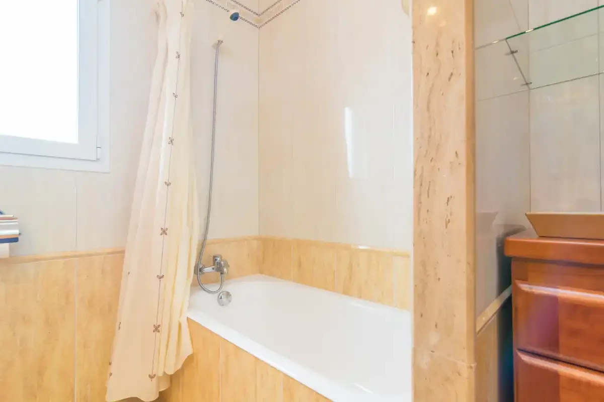 A bathroom with a bathtub, shower curtain, and wooden vanity.