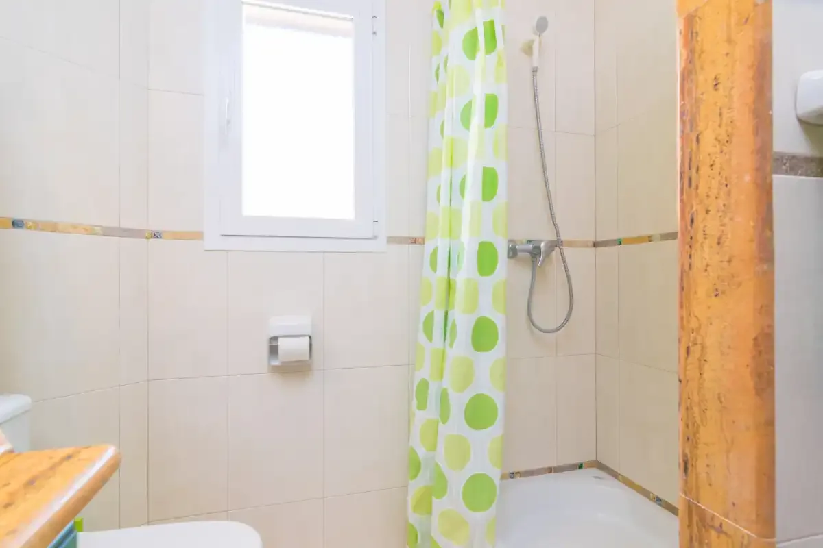 A tiled bathroom with a shower and a green patterned curtain.