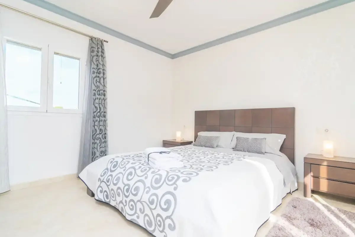 A bright bedroom with a large bed, patterned bedding, and matching bedside tables.