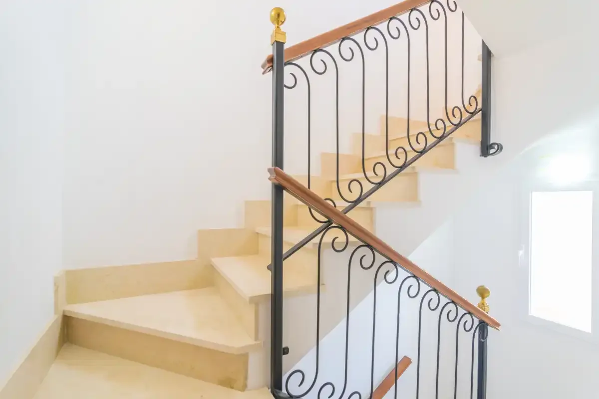 A bright interior staircase with pale steps and decorative metal railings.