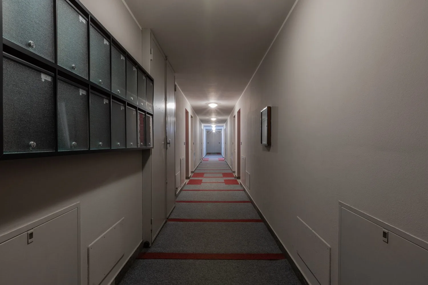 Un largo pasillo interior con buzones en una pared y una alfombra con franjas.