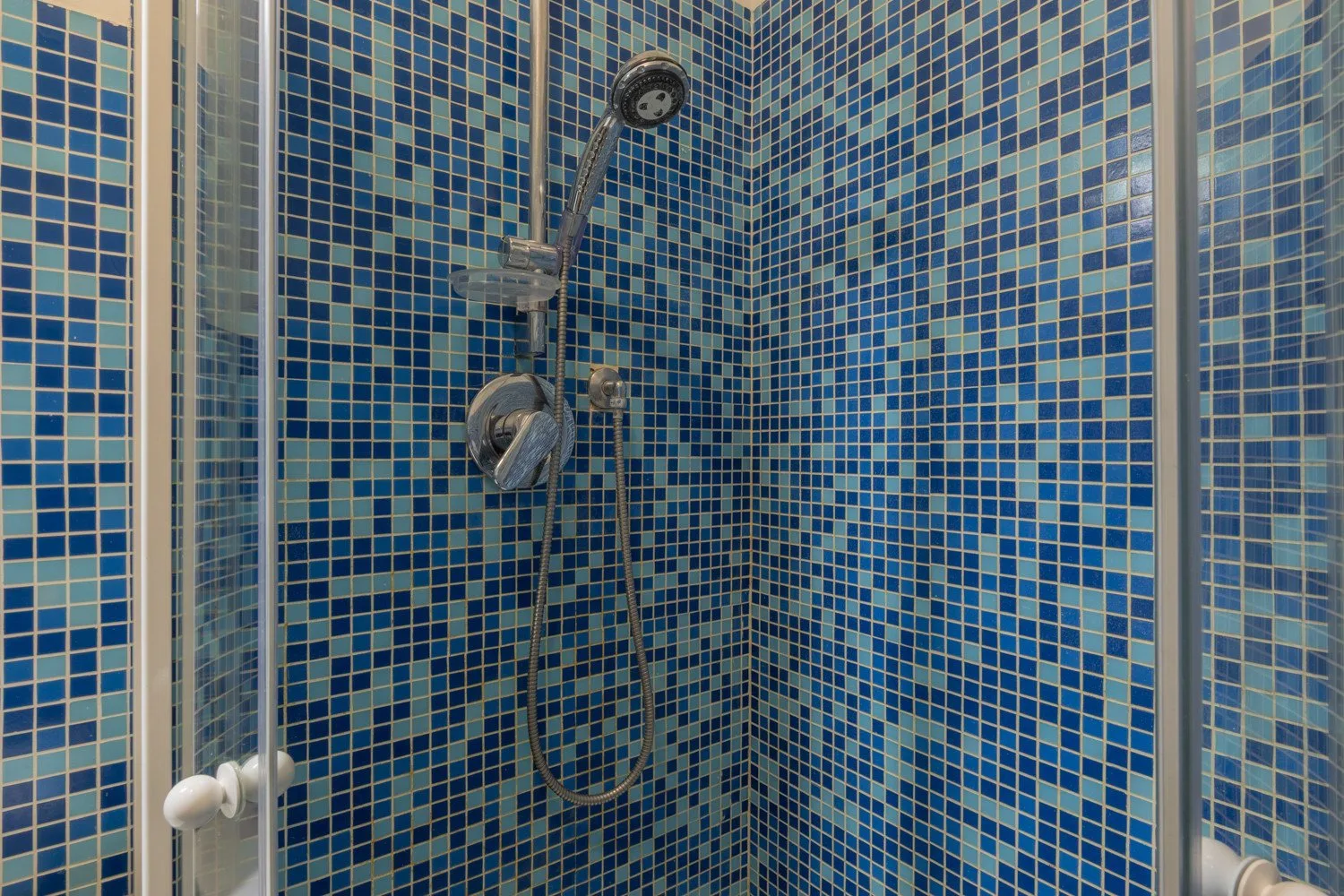 Una ducha con azulejos, ducha de mano y controles.