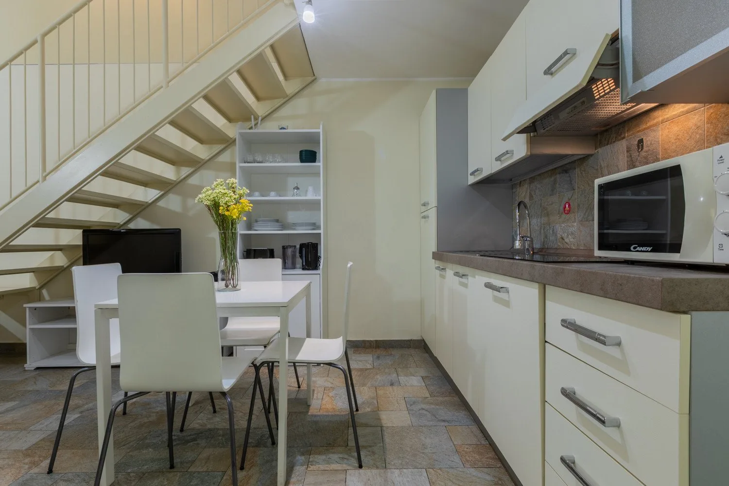 Una cocina con zona de comedor, armarios, una mesa y una escalera.
