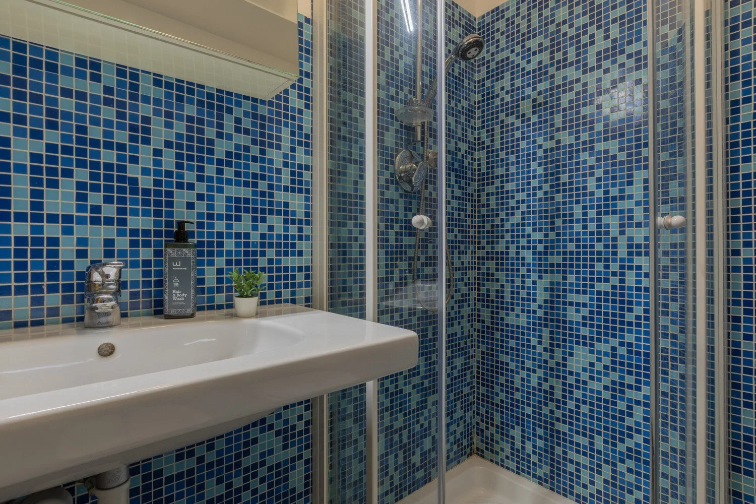 Un baño con paredes de mosaico azul, un lavabo y una ducha de vidrio.