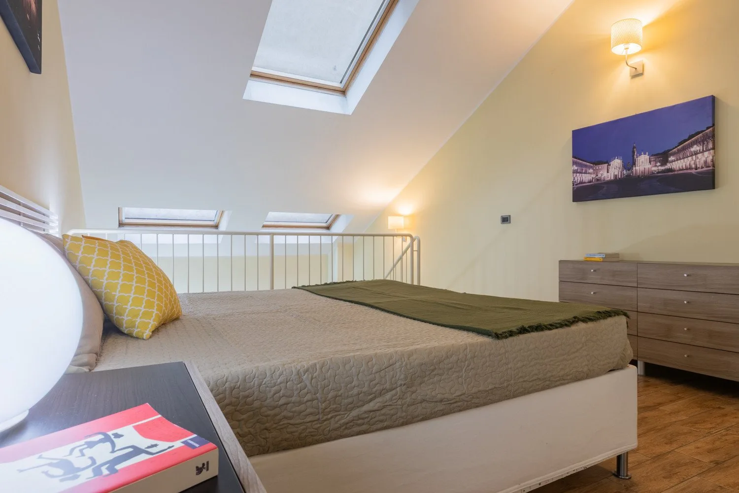 Un dormitorio con una cama bajo un techo inclinado y una claraboya.