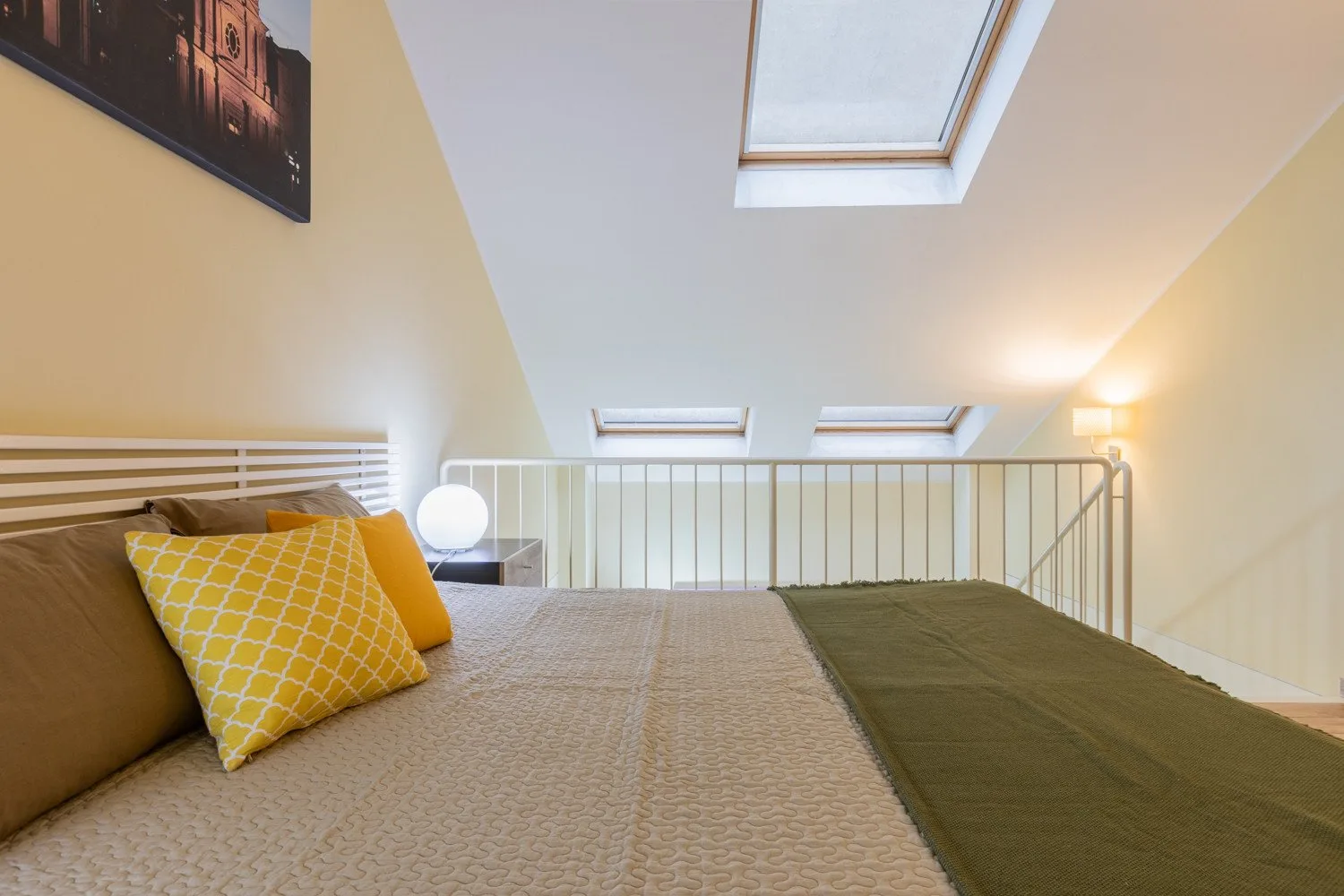 Una cama está bajo paredes inclinadas y tragaluces en un dormitorio luminoso.