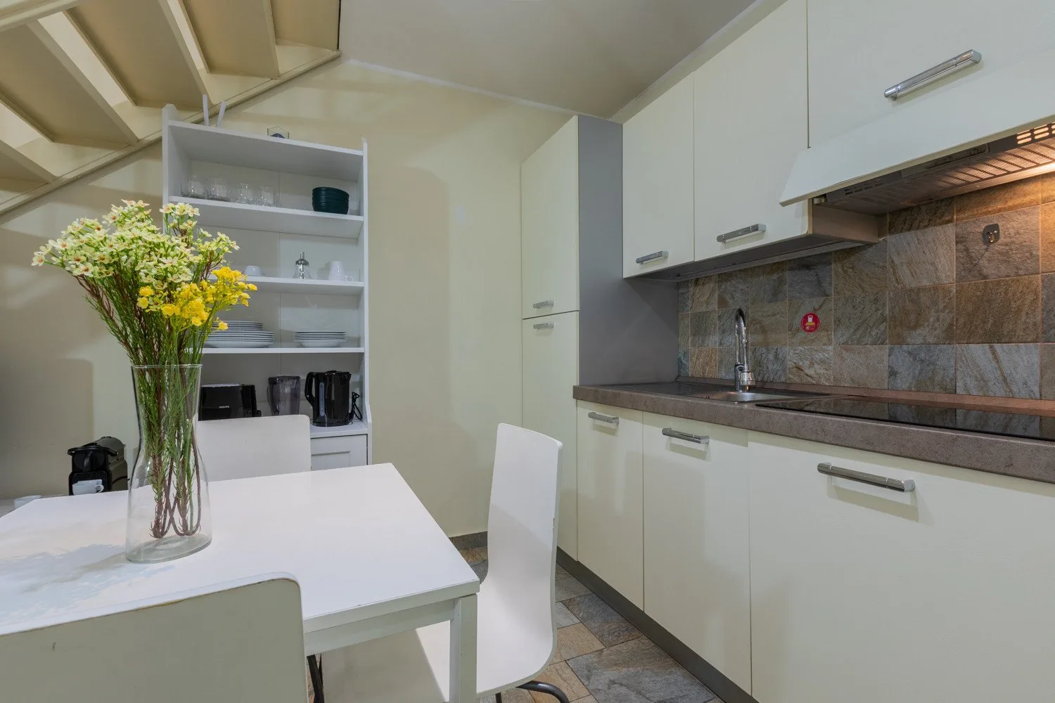 Cocina luminosa con armarios blancos, una encimera y una mesa de comedor con flores.