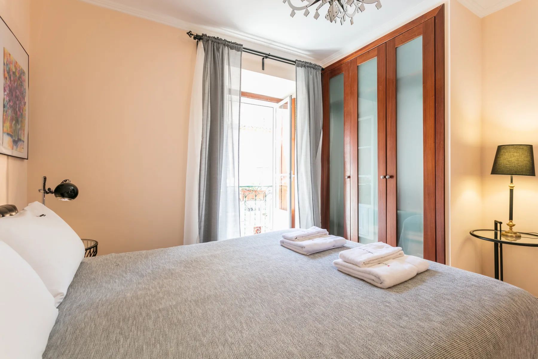 A bedroom with a neatly made bed, folded towels, and a wardrobe.