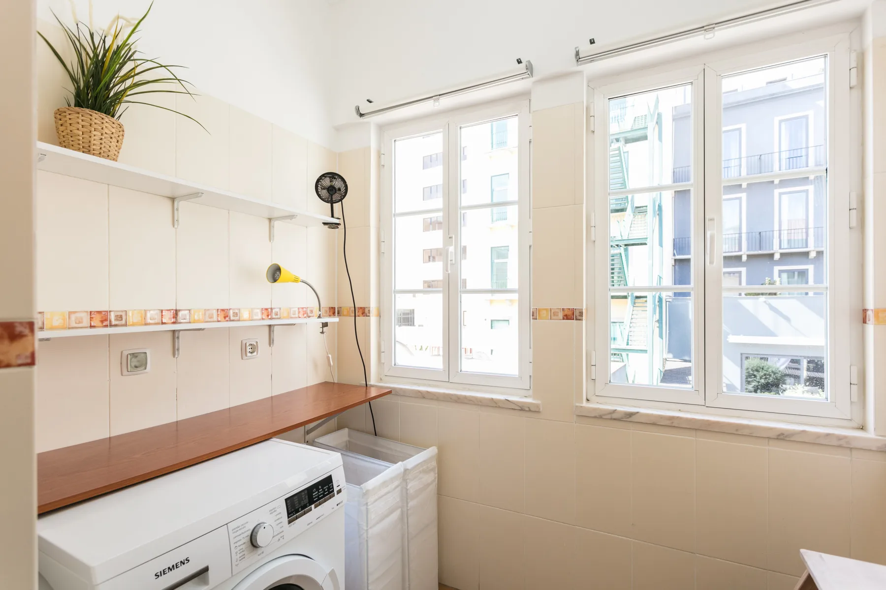 A bright laundry room with a washing machine beneath large windows.