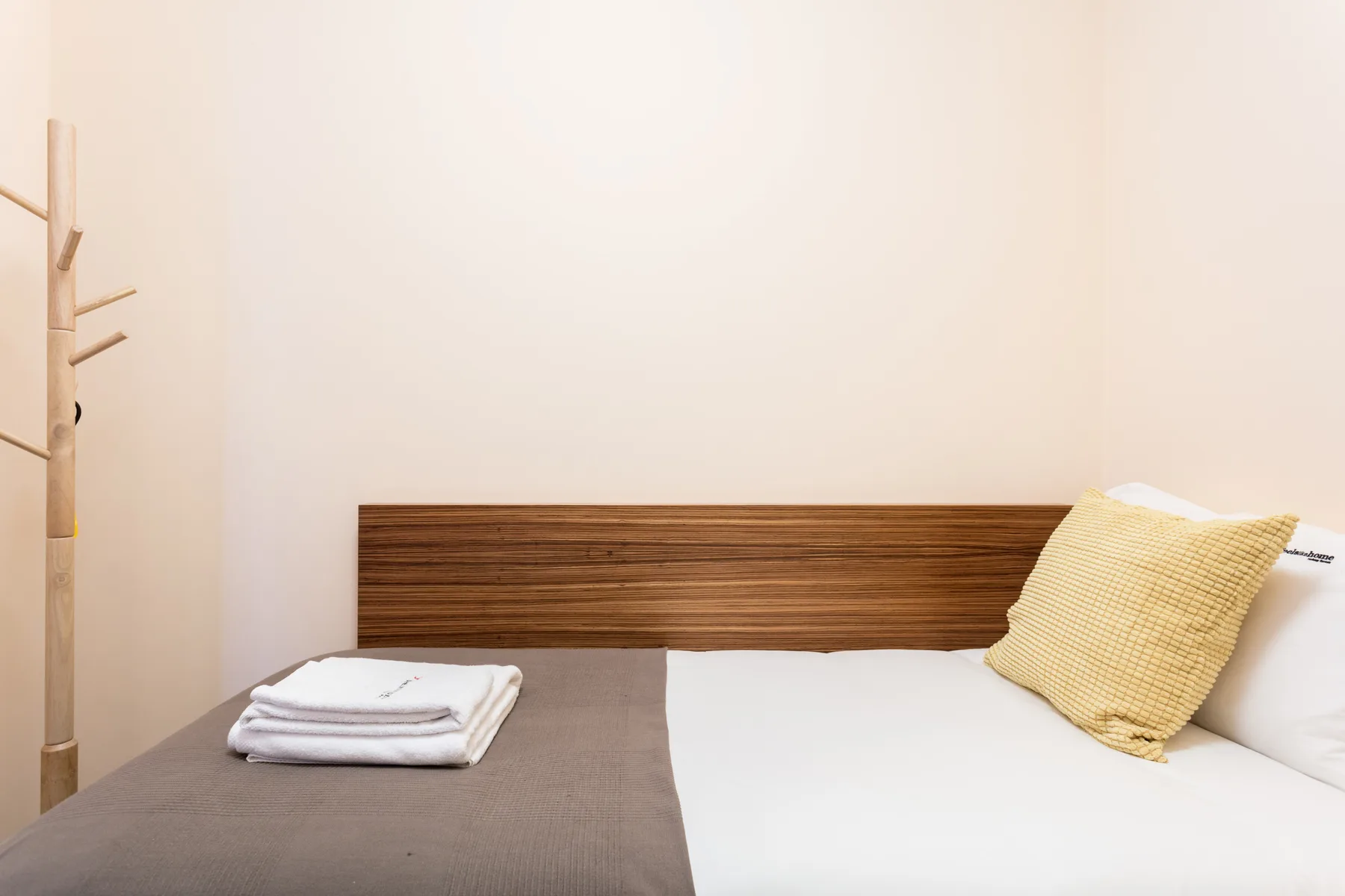 A bedroom with neatly folded towels on the bed beside a wooden headboard.