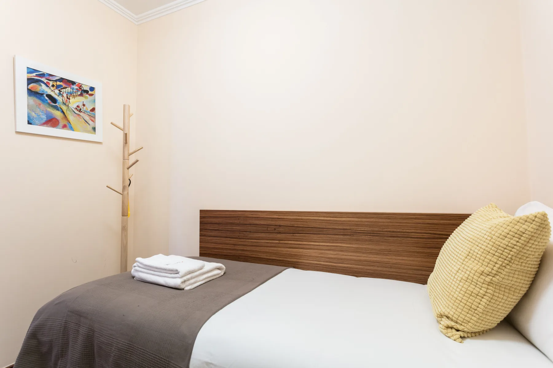 A bedroom with a bed, folded towels, and a framed picture on the wall.