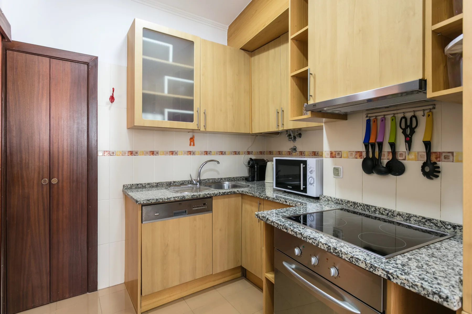 A compact kitchen with wood cabinets, granite counters, and a built-in cooktop.