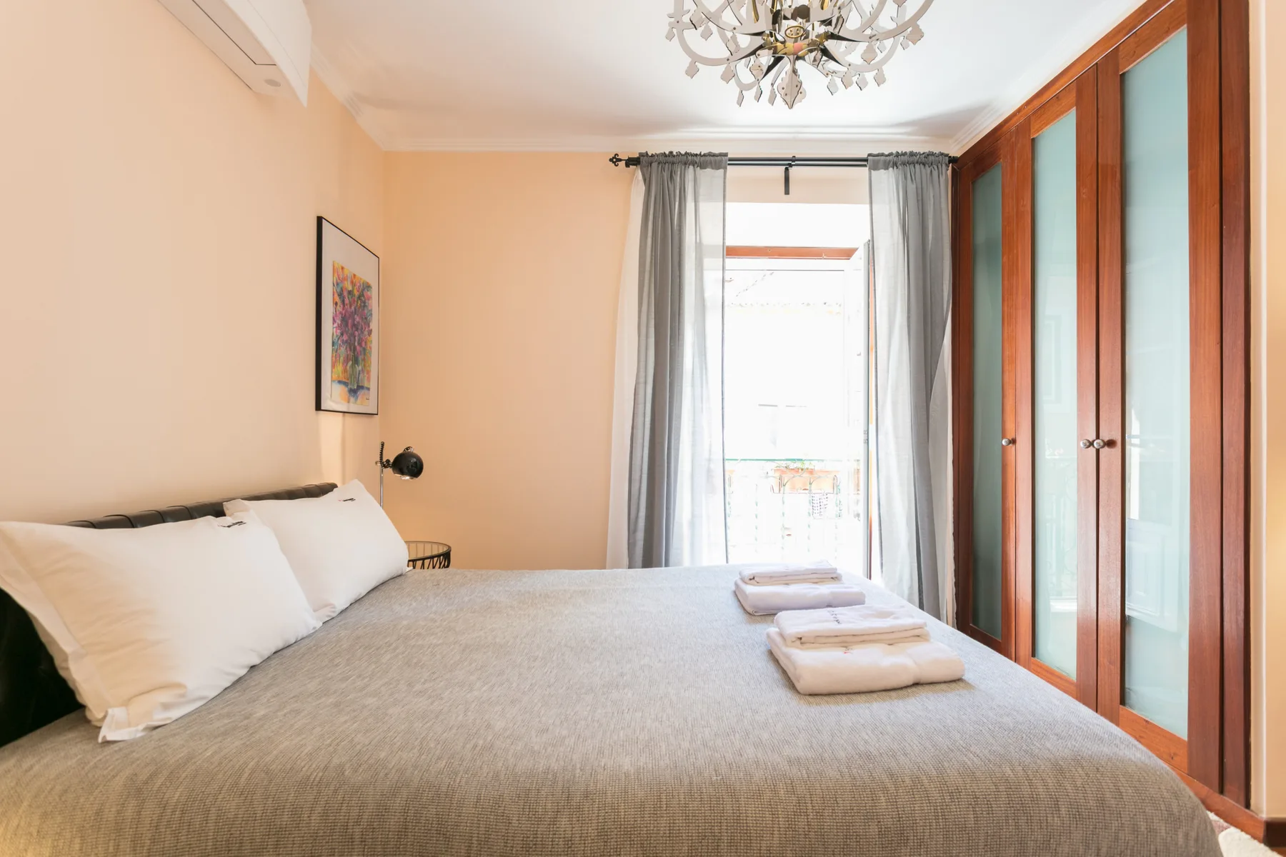 A bedroom with a bed, folded towels, and glass-paneled doors.