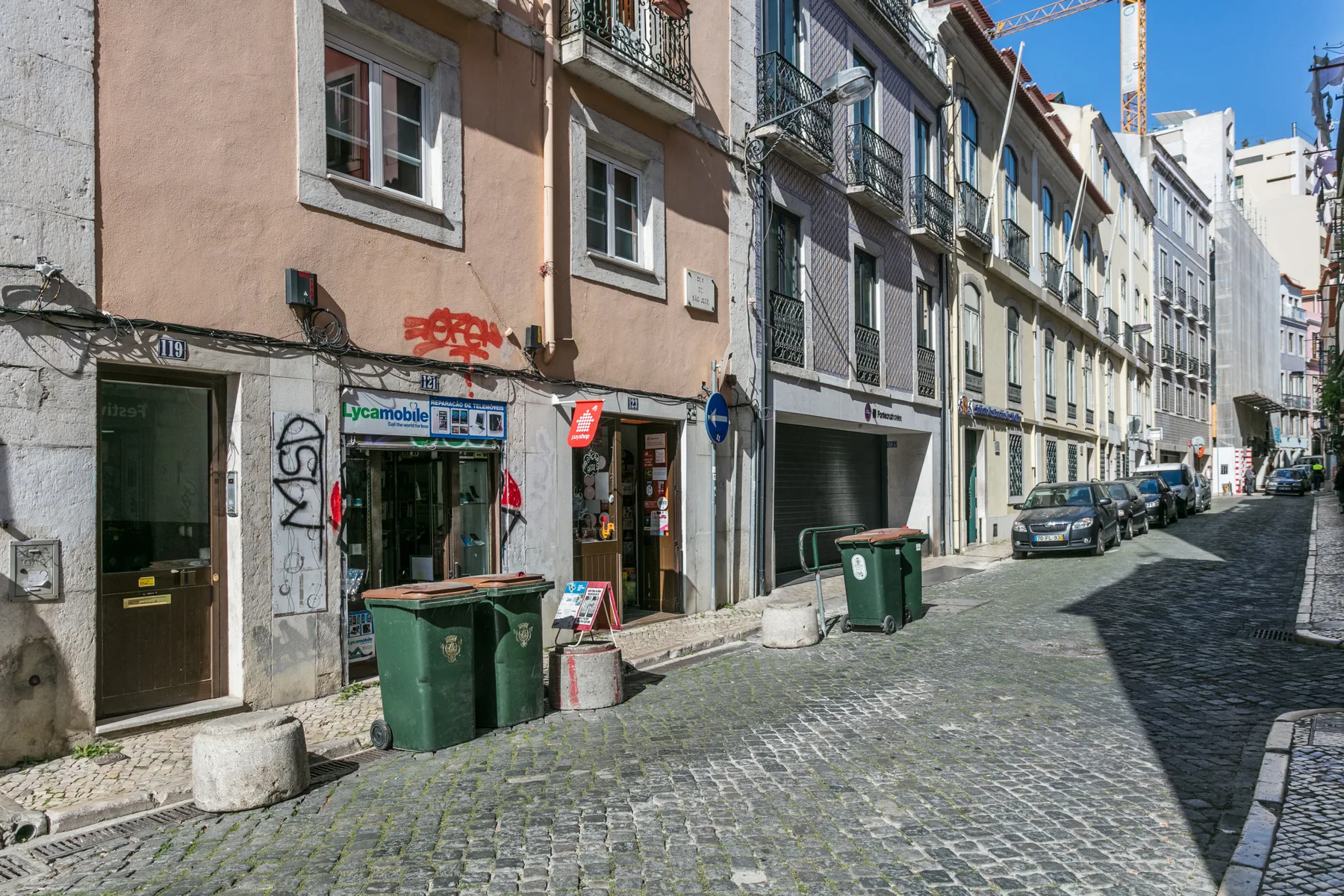 A cobblestone city street lined with apartment buildings and parked cars.