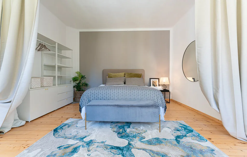 Un dormitorio con una cama, ropa de cama estampada y una gran alfombra azul y blanca.