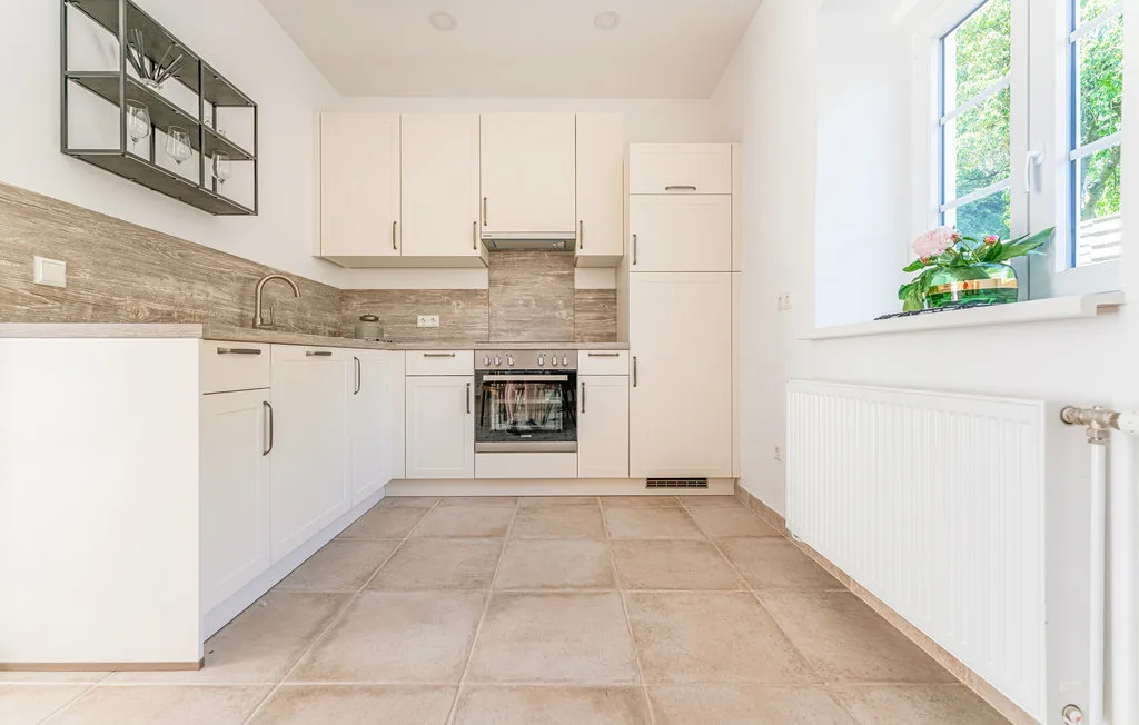 Una cocina luminosa con armarios blancos, un horno y una ventana grande.