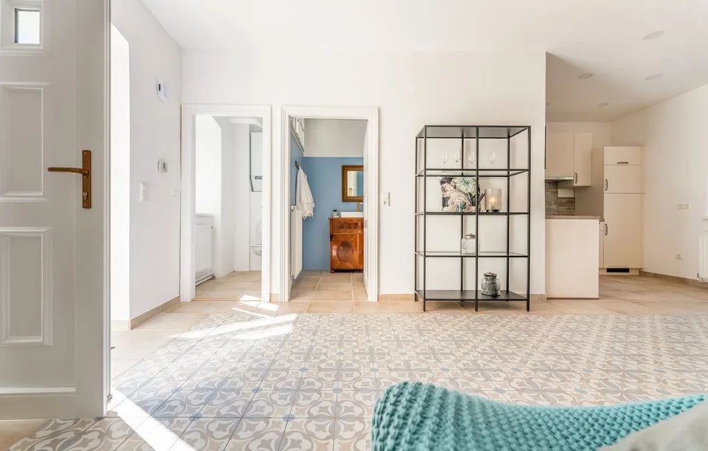 Un interior luminoso con suelo de baldosas estampadas, estanterías y una pequeña zona de cocina.