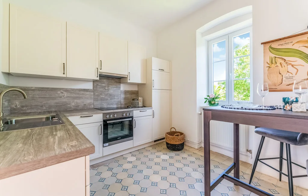 Una cocina luminosa con gabinetes claros, suelo estampado y una mesa junto a la ventana.