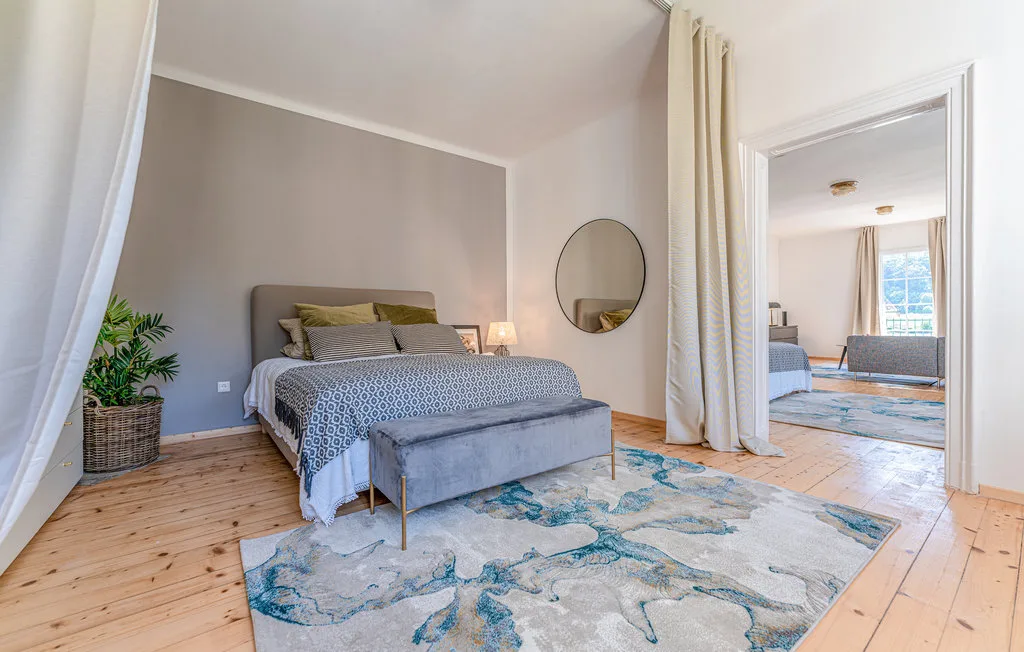 Un dormitorio con una cama, una alfombra estampada y cortinas que dan a una zona de estar.